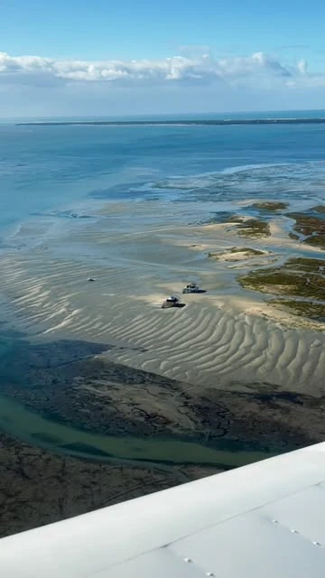 Des bancs de sable dessinent des ondulations dans la mer, vus depuis un avion.