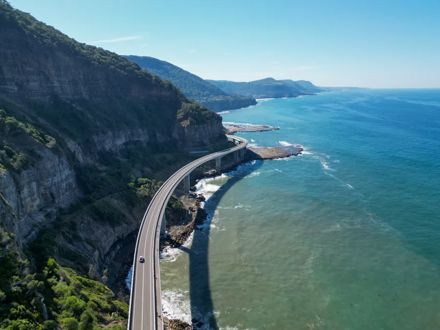 Une route sinueuse longe une falaise et une mer bleu profond.