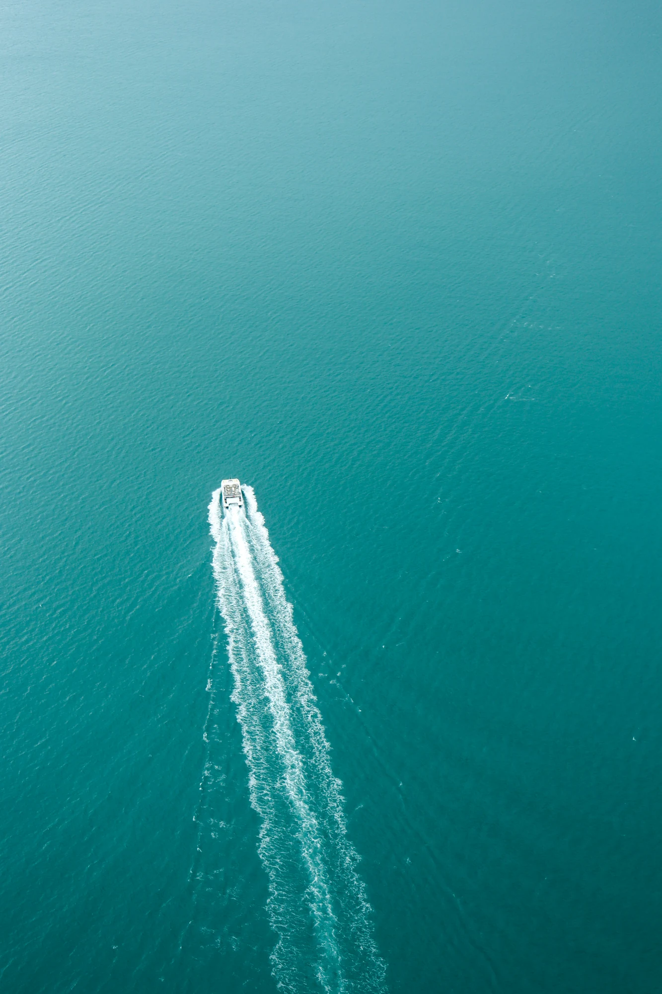 Un petit bateau dessine un sillage blanc sur une mer turquoise.