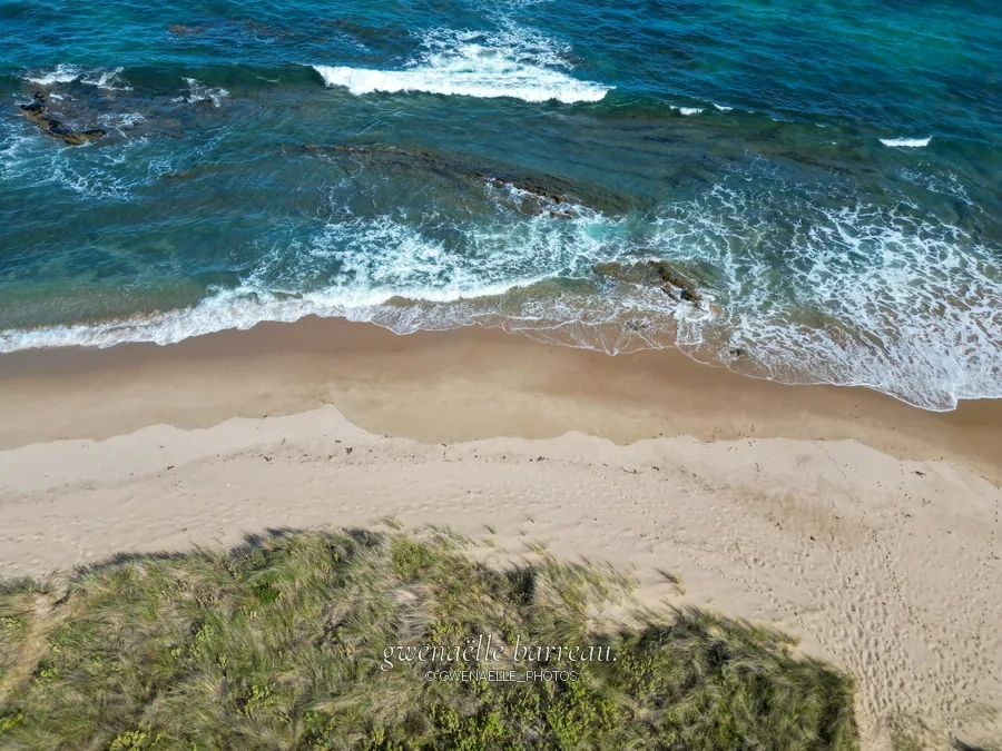 Vue verticale des vagues turquoise qui rejoignent une plage de sable clair.