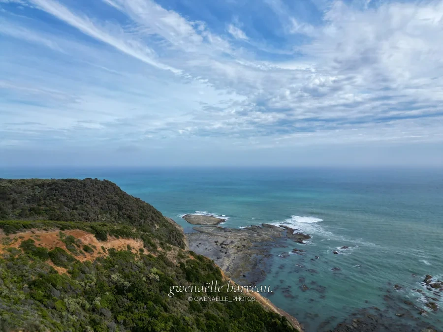Falaises végétalisées et récifs côtiers sous un ciel parcouru de nuages.