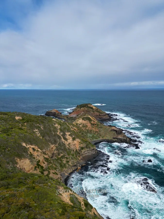 Côte rocheuse découpée et vagues blanches sous un ciel couvert.