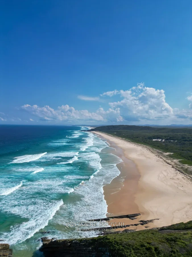 Lignes de vagues blanches le long d'une grande plage de sable.
