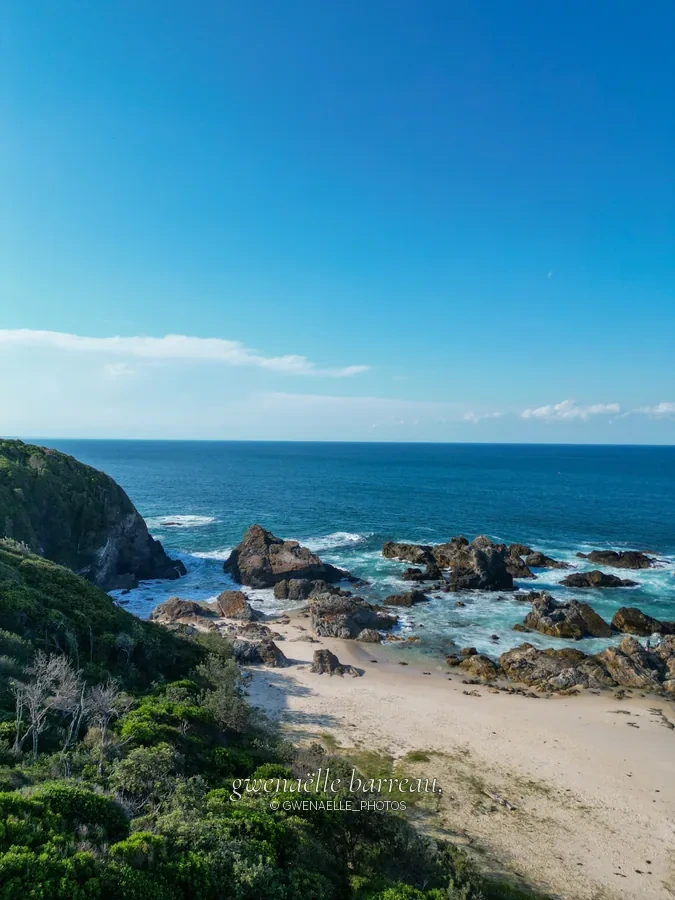Petite plage et rochers abrités par une végétation côtière dense.