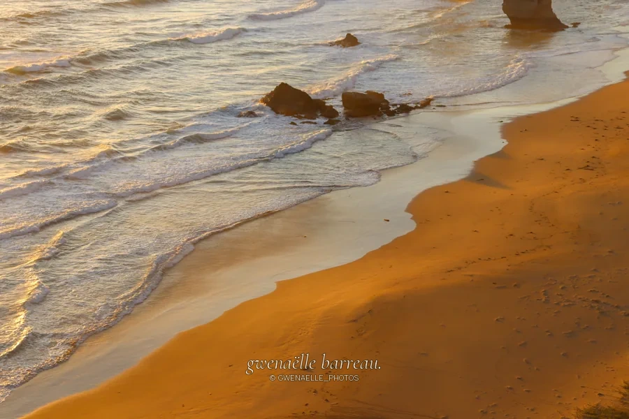 Vagues dorées et rochers sur une plage dans une lumière chaude.