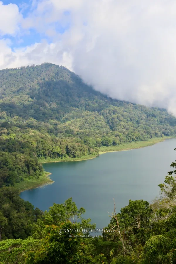 Lac bordé de versants verdoyants sous des nuages bas.