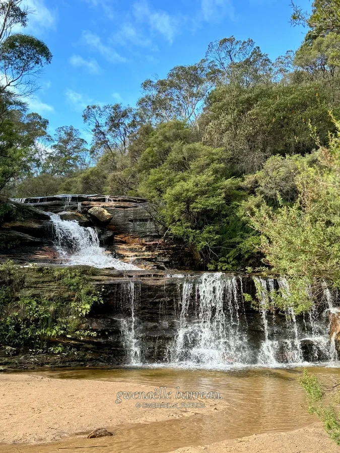 Cascade étagée sur des rochers au milieu des arbres.