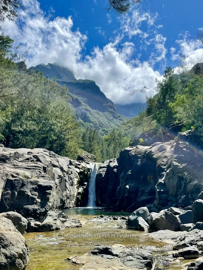Rivière et petite cascade entre des rochers dans une vallée montagneuse.