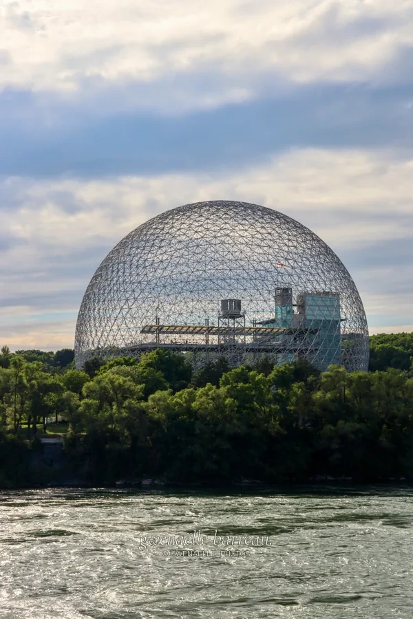 Grande structure sphérique ajourée au-delà des arbres et de l'eau.