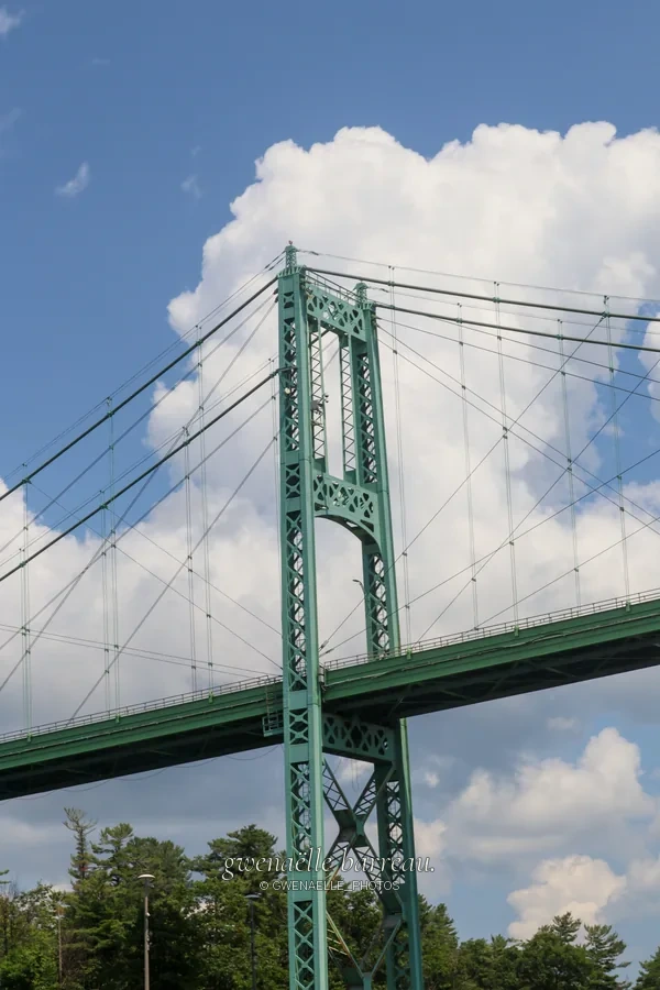Tour et câbles d'un pont suspendu vert sous des nuages blancs.