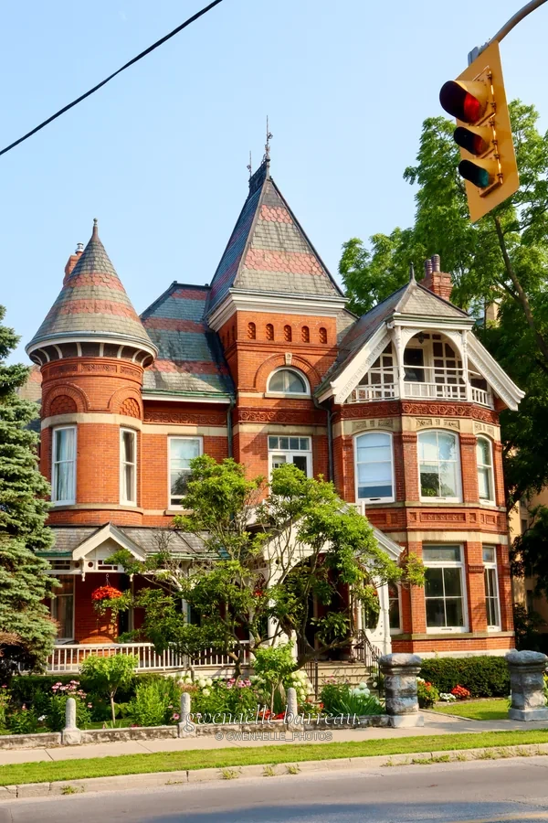 Grande maison en brique avec tourelles et façade ouvragée au bord d'une rue.