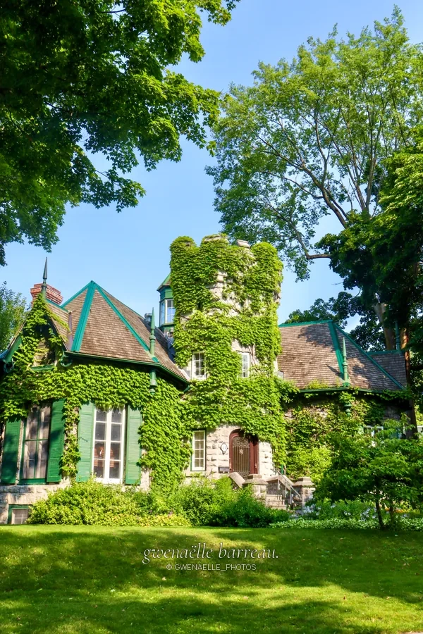 Maison en pierre au toit pointu dans un jardin arboré.