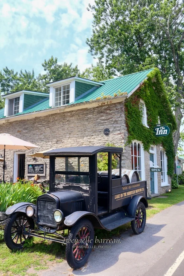 Voiture ancienne noire devant une maison et sa façade végétalisée.