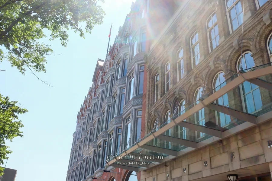 Façade de pierre et marquise vitrée éclairées par le soleil.