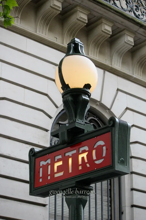 Enseigne rouge « Métro » sous un globe lumineux et une façade de pierre.