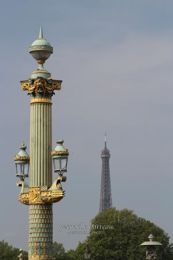 Lampadaire ouvragé aux détails dorés devant une tour métallique lointaine.