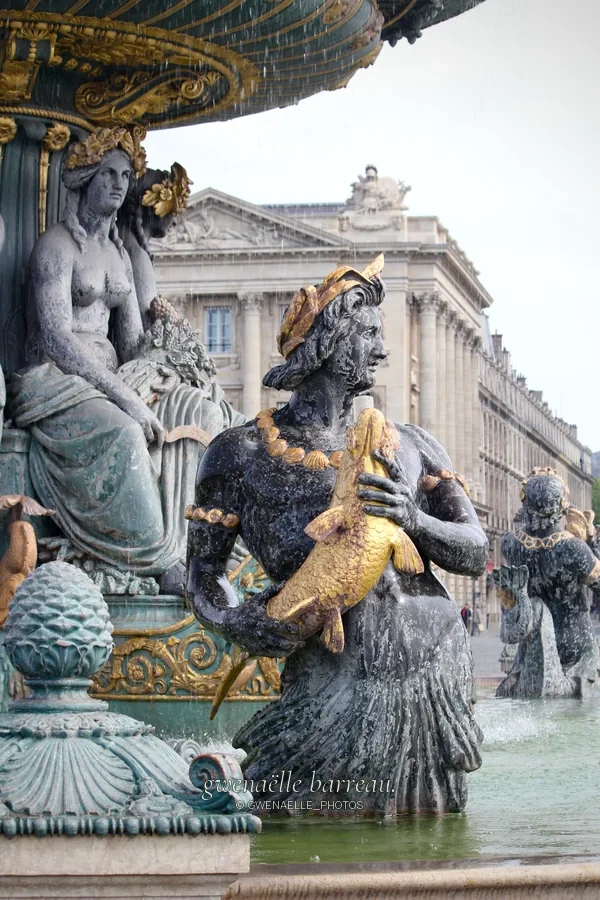 Statues et ornements dorés d'une fontaine devant un bâtiment à colonnes.