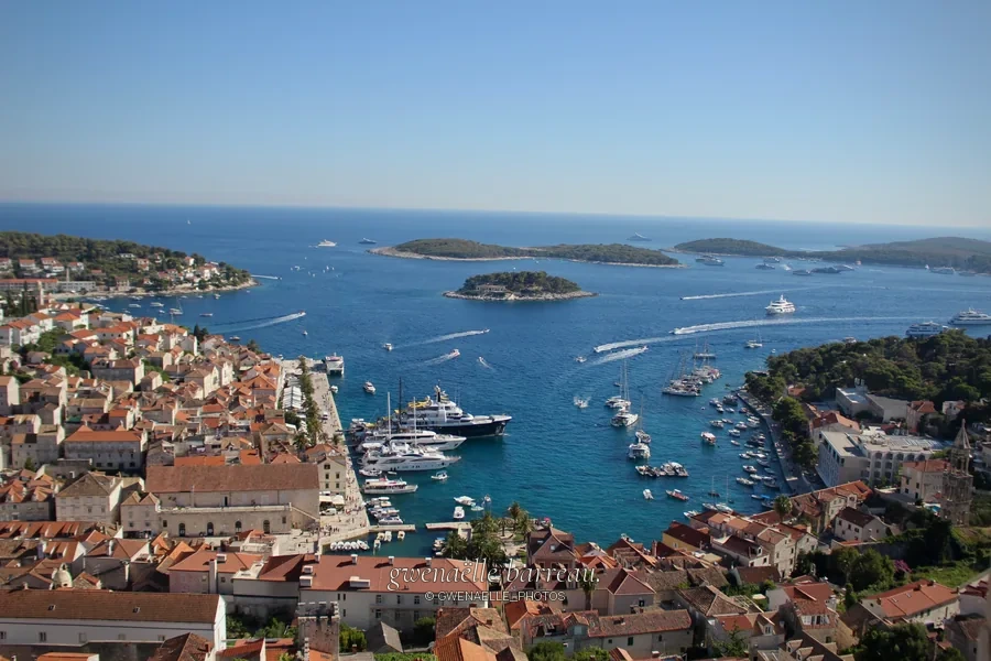 Baie bleue et bateaux entourés de maisons aux toits orangés, vus en hauteur.