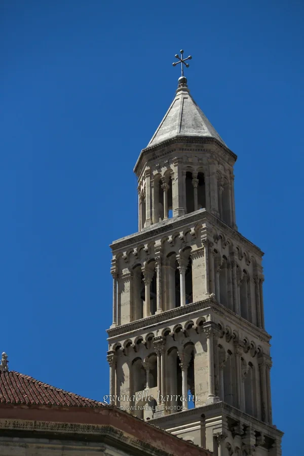 Haut clocher de pierre à arcades sous un ciel bleu.