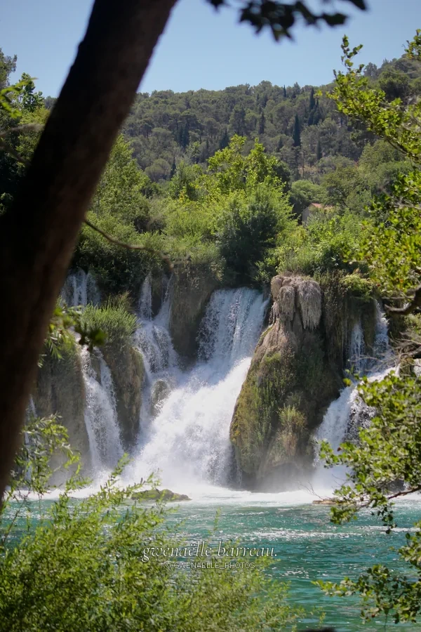 Chute d'eau et bassin turquoise encadrés par des arbres.