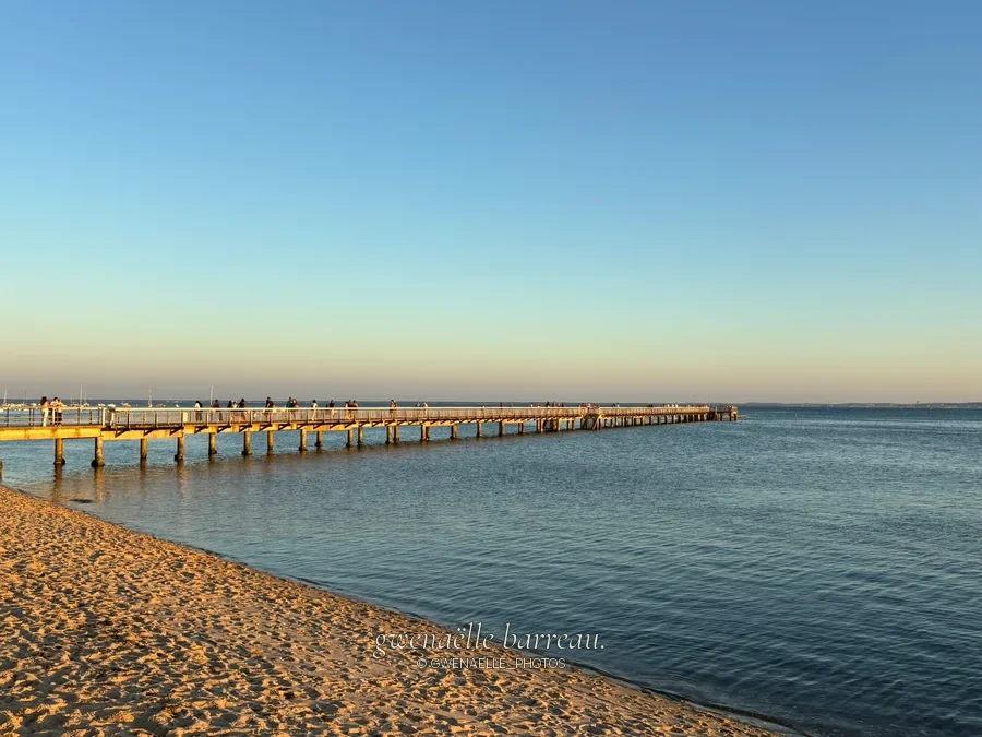 Jetée s'avançant dans une mer calme depuis une plage de sable.