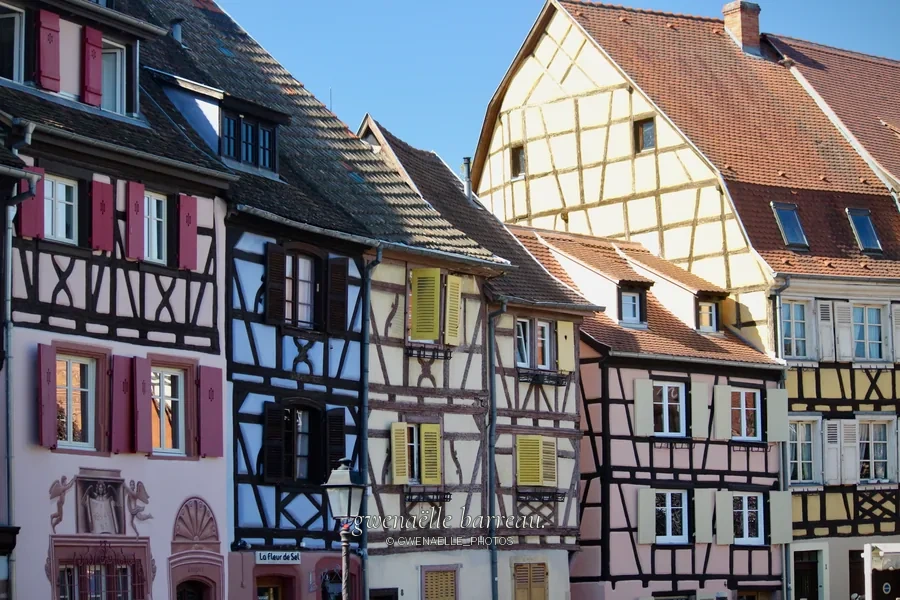 Façades à colombages et toitures inclinées sous un ciel bleu.